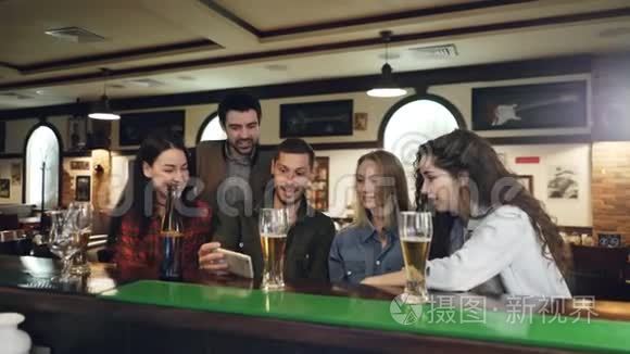 英俊的大胡子正在智能手机上向他的朋友们展示视频，同时一起在酒吧放松。 年轻人