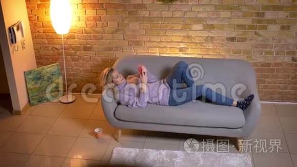 在舒适的家里躺在沙发上用手机拍摄白种人成年金发女性的特写镜头