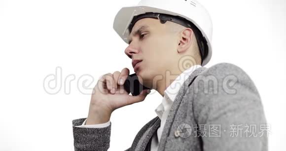 严肃的商人戴着白色建筑头盔，在白色背景下的手机上交谈。