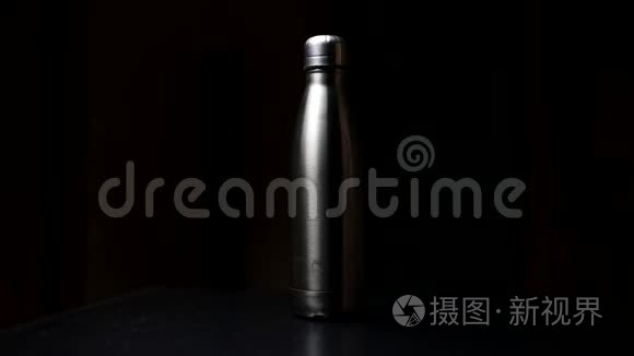 特写男性手采取可重复使用，钢热水瓶从桌子上黑色工作室背景。