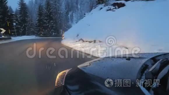 现代汽车，车前灯在道路上沿雪覆盖的树木和山丘。