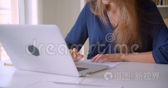 年轻有魅力的高加索女商人用笔记本电脑在室内做笔记的特写照片