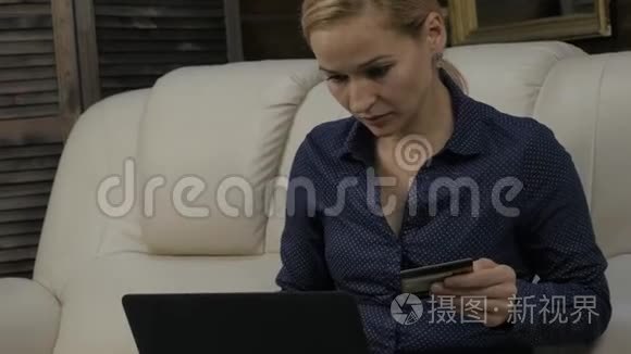 漂亮的女人坐在家里的沙发上，用笔记本电脑和银行信用卡在线购物。 4K