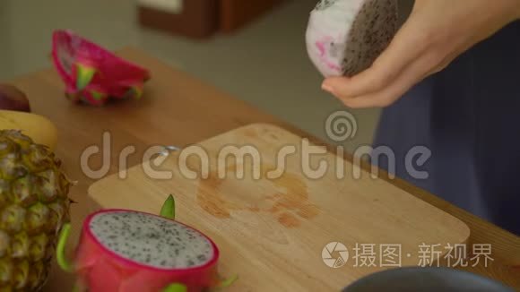 慢镜头一位年轻女子将火龙果切成方块状，许多热带水果摆在桌上
