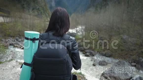 徒步旅行者女士背着背包在山上和山河湖上寻找，女孩在旅途中欣赏大自然的全景