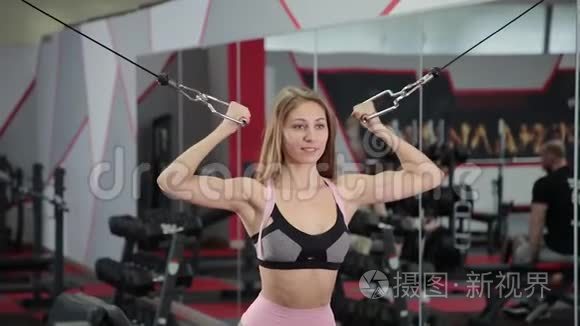 漂亮的运动年轻女孩在健身房的块模拟器上训练二头肌。