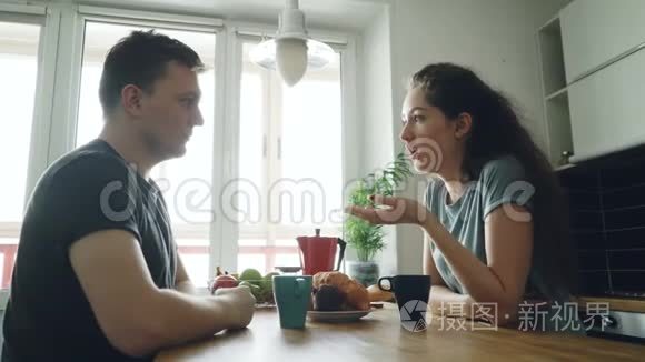 年轻的白种人夫妇坐在现代宽敞明亮的厨房里，用积极的方式讨论一些事情，他们是