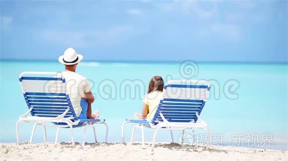 父亲和女儿在热带海滩上坐在躺椅上，欣赏着大西洋的景色