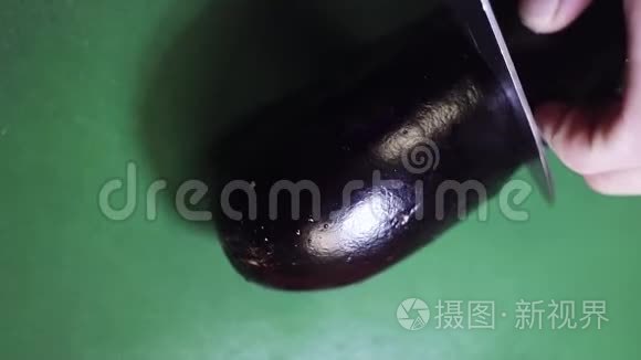 绿色餐桌上用锋利的大刀切割茄子的俯视图。