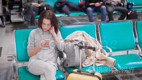 在飞机起飞前，独自一人的年轻女子坐在机场候机室的椅子上，在她的手机着留言