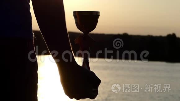 日落时分，男人的手在湖岸上捧着一个胜利者的碗
