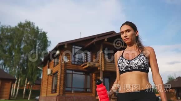 运动的女人，在一个木制豪宅的背景下，一个漂亮的压在黑色顶部的美女，锻炼了饮用水