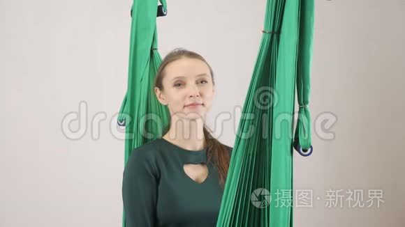 年轻的女人坐在吊床上，微笑的女人展示着手掌的标志。 空中航空飞行健身教练训练。 冥想