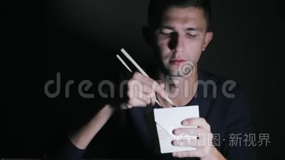 一个从盒子里拿筷子吃面条的男人的特写。 欧洲人吃中国菜