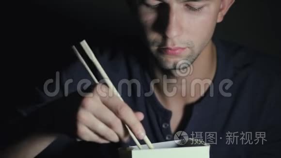 一个从盒子里拿筷子吃面条的男人的特写。 欧洲人吃中国菜