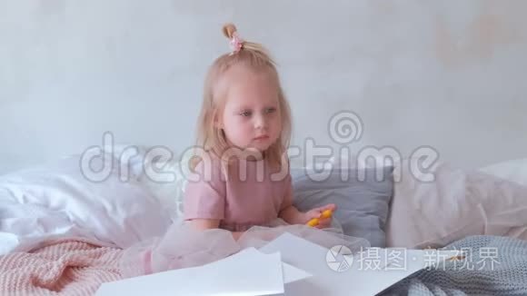 小可爱的金发女孩穿着粉红色的连衣裙，手里拿着一只毛毡笔，坐在纸上。