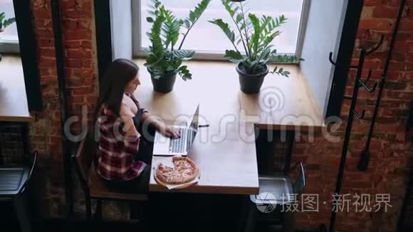 漂亮迷人的商务女性在咖啡馆里的笔记本电脑后面工作，桌子上有披萨。
