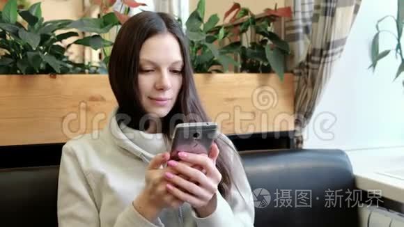 快乐的年轻黑发女人正在考虑一些有趣的事情，在咖啡馆里玩手机