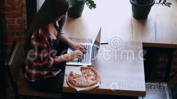 漂亮迷人的商务女性在咖啡馆里的笔记本电脑后面工作，桌子上有披萨。