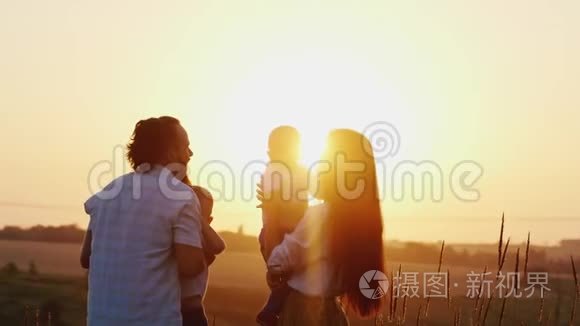 年轻的男女和年幼的孩子玩耍，在夕阳的背景下把他们抛在空中