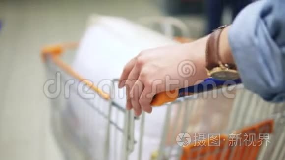 在超市里`一个女人的手拿着一辆手推车，推着一辆手推车。 背面视图
