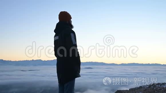 从后面看。 一个孤独的人站在高高的山上，看着夕阳和夕阳的地平线
