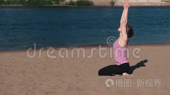 在城市河边的海滩上伸展瑜伽的女人。美丽的城市景色。呼吸练习。