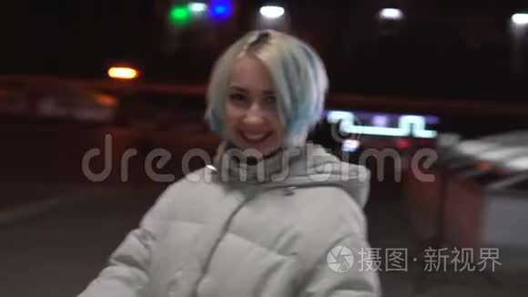 美丽的年轻女子对抗黑夜闪耀的城市。 金发女郎在夜城里走来走去