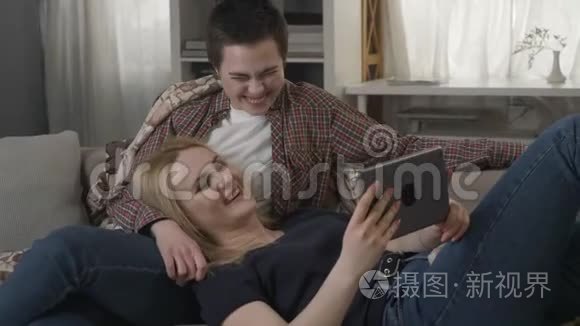 女夫妇正在沙发上休息，用平板电脑和笑声，年轻的家庭，格子，舒适的60fps