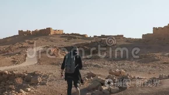 带背包的人在古老的废墟中徒步旅行。 放松的欧洲男性旅行者走在沙漠岩石和沙子上。 以色列4K.