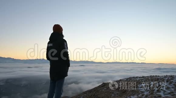 从后面看。 一个孤独的人站在高高的山上，看着夕阳和夕阳的地平线