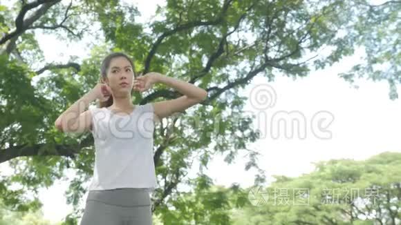 运动的年轻亚洲女人在公园日出前热身和伸展运动。