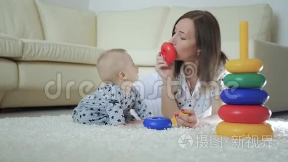 快乐的妈妈和宝宝在家里地毯上玩玩具。 侧面看一对快乐的母子玩玩具