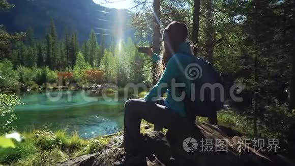 年轻的女游客背着背包坐在石头上，正在欣赏美丽的蒙丹湖的风景。