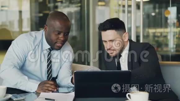 两位商务同事正在看手提电脑，并在玻璃墙的现代办公室讨论他们的项目