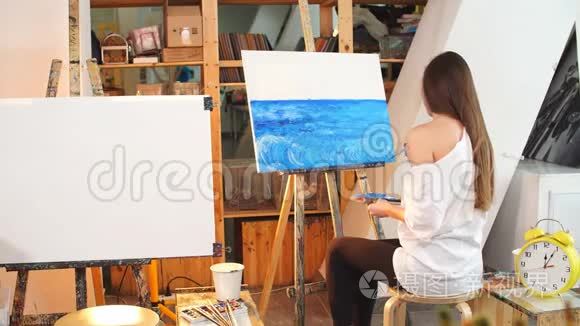 一位年轻的女艺术家在她的车间里用蓝色油画颜料在画布上作画。