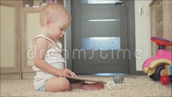 带着平板电脑的小男孩坐在家里的地板上，在室内。 幼儿帅哥玩屏幕