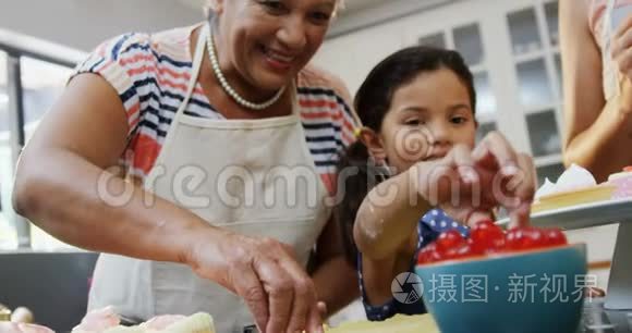 女孩一边吃樱桃一边和妈妈和奶奶做蛋糕