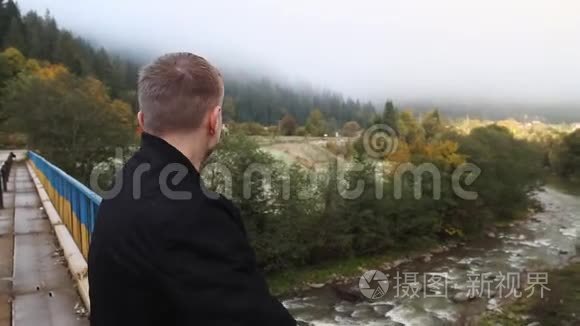 一个年轻人在雾中从桥上望向山河和山