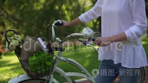 女人的近景她手里拿着一辆城市自行车的车把，手里拿着一个花篮和一本书。 女人享受着