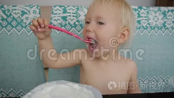 宝宝吃酸奶弄得一团糟。笑着的白人蓝眼睛女婴吃酸奶的肖像。