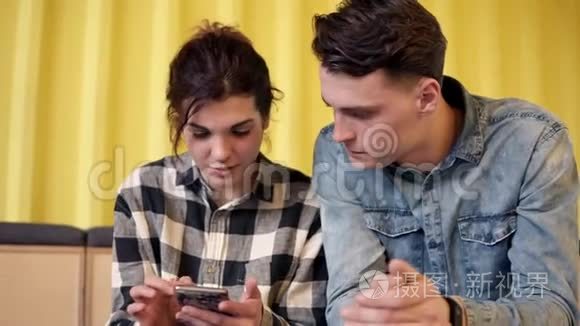 一对夫妇坐着聊着什么。 年轻迷人的女孩在她的智能手机上给她的男朋友看一些东西。