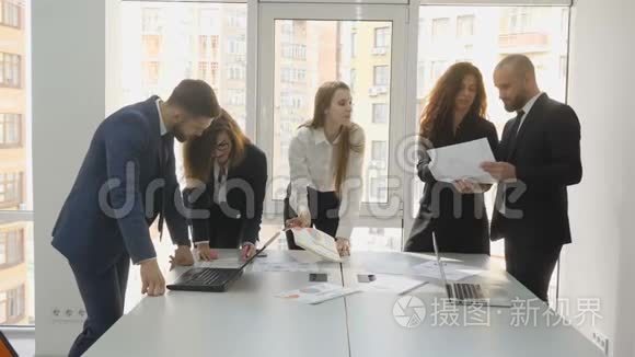 办公室工作人员站在一张桌子旁讨论公司的财务问题，一支由三名妇女和两名男子组成的年轻团队