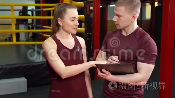 肌肉教练在剪贴板上写字，在交叉训练体育馆和年轻女子交谈