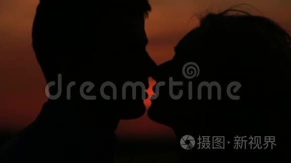 这对迷人的剪影夫妇在夕阳红的天空背景下轻轻亲吻的特写肖像。