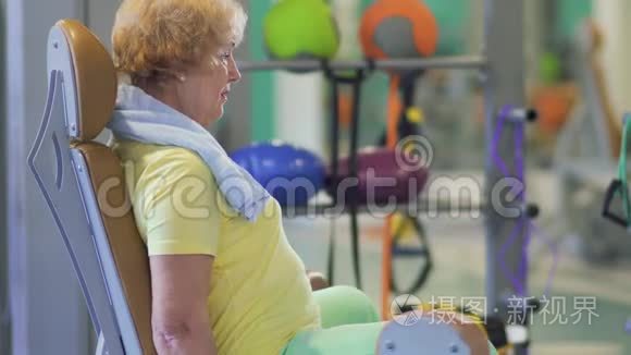 快乐的奶奶在健身房训练她的腿，并在摄像机上显示拇指