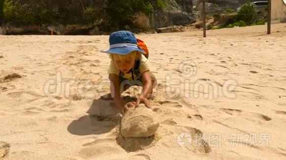 印度尼西亚巴厘岛上，一个顽固不化的小男孩推着一块大石头在海浪滚滚的海滩上