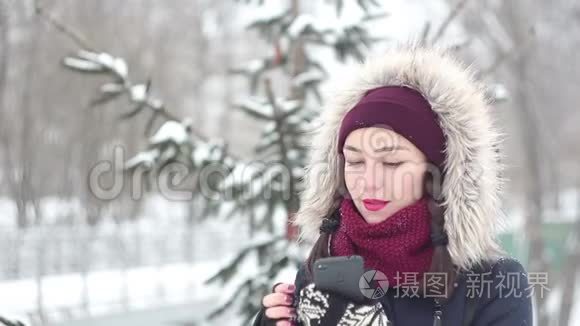 美丽的年轻女孩在冬天的公园里散步时，在她的智能手机上说话。