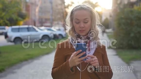 幸福的金发年轻女子正在通过耳机听音乐，穿过秋天的城市。 瞬间