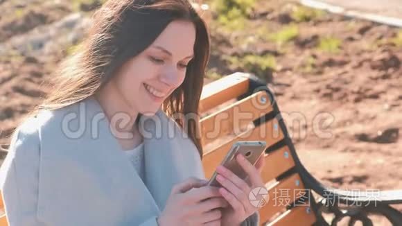 一幅快乐的黑发女人坐在公园的长凳上，在手机上阅读和键入一条信息的肖像。